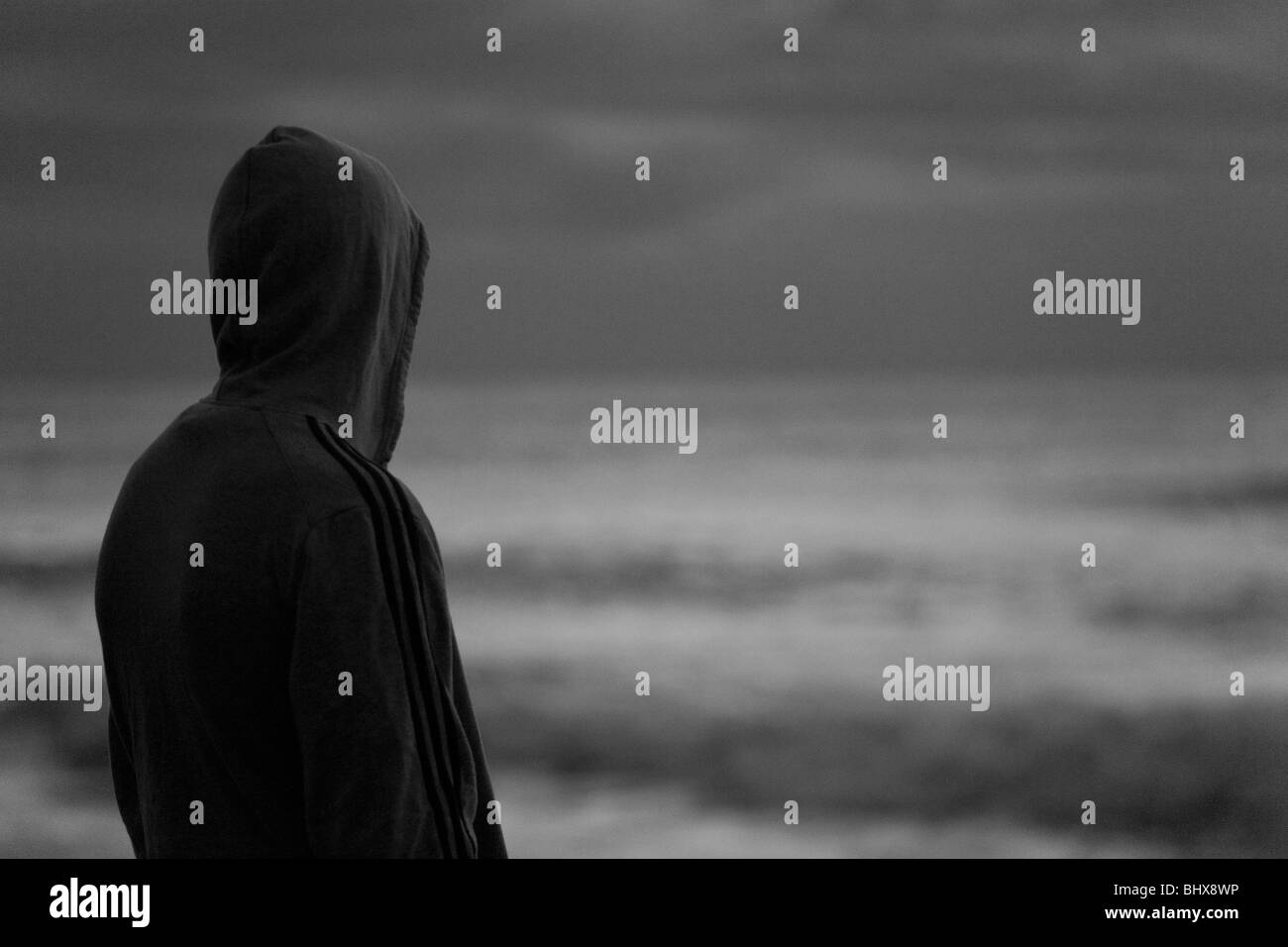 Hooded figure looks out to sea Stock Photo