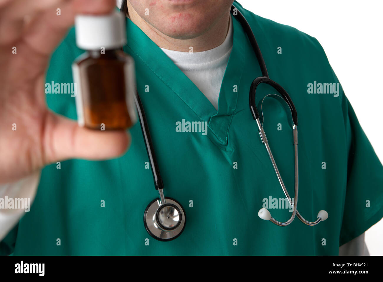 man wearing medical scrubs and stethoscope holding and looking at a small bottle of pills Stock Photo