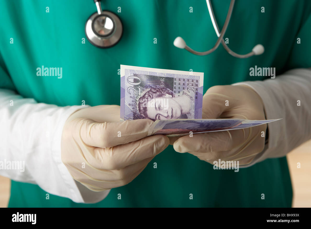 man wearing medical scrubs and stethoscope counting 20 pounds sterling banknotes Stock Photo