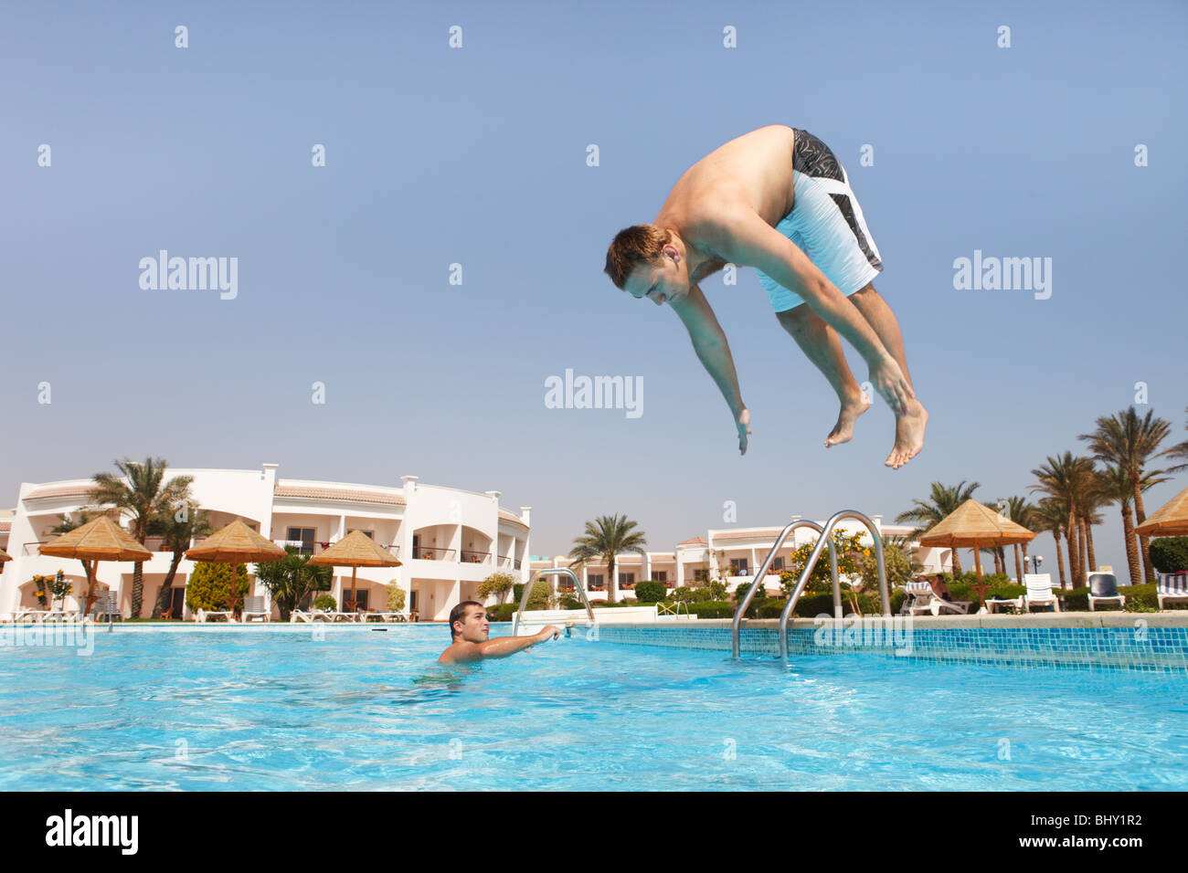 Two men jumping in swimming pool. Low angle view from the swimming pool ...