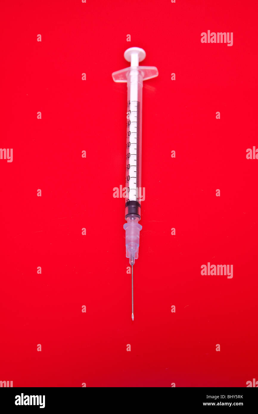 Needle and syringe on a red studio background. Stock Photo