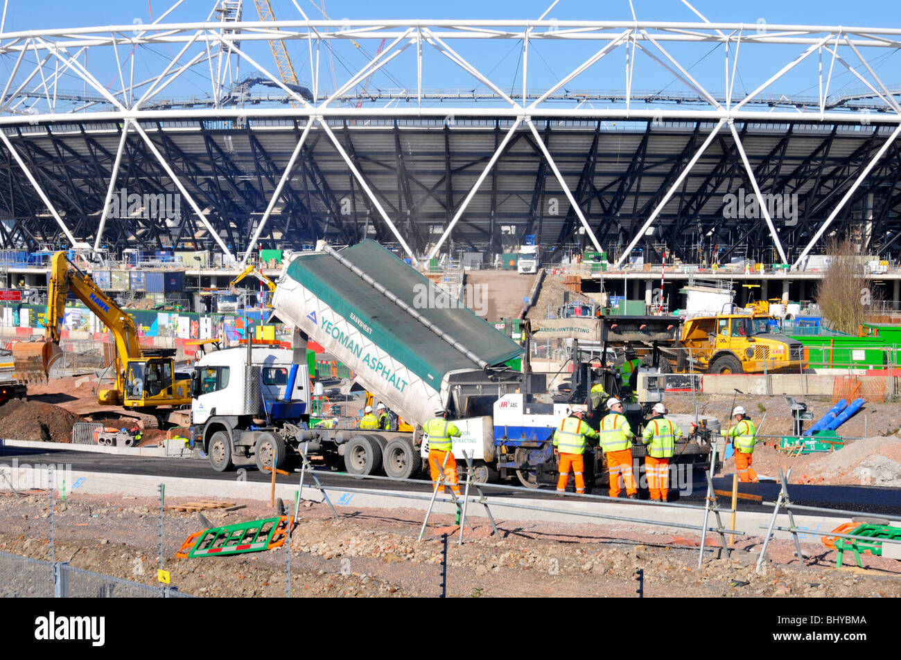 2012 East London Olympic Games stadium construction building site asphalt road work tarmac machine & lorry truck group of workers Stratford England UK Stock Photo