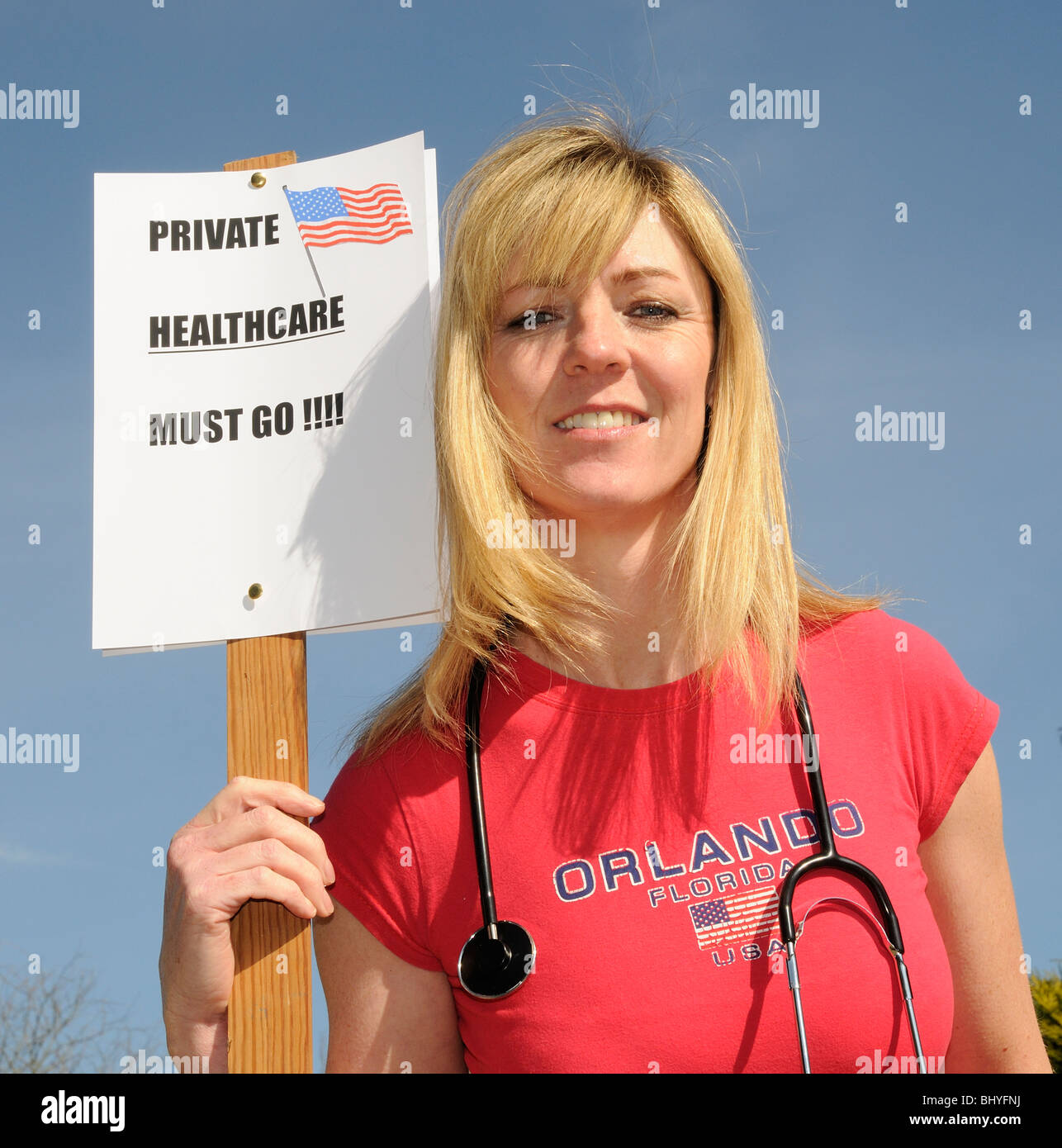 Private healthcare in the USA must go female protester wearing red shirt and holding a stethoscope Stock Photo