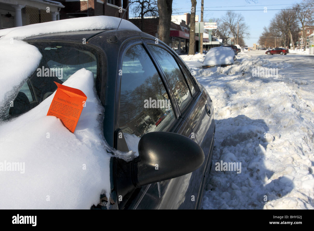 Parking ticket embedded in snow on car windshield on snowy street. Stock Photo