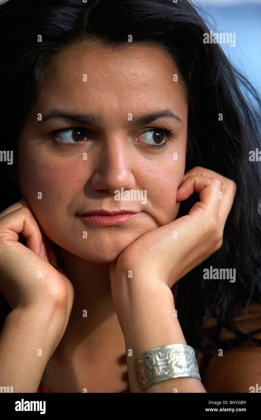mid twenties hispanic woman resting her chin on her palms sitting bored waiting looking away watching Stock Photo