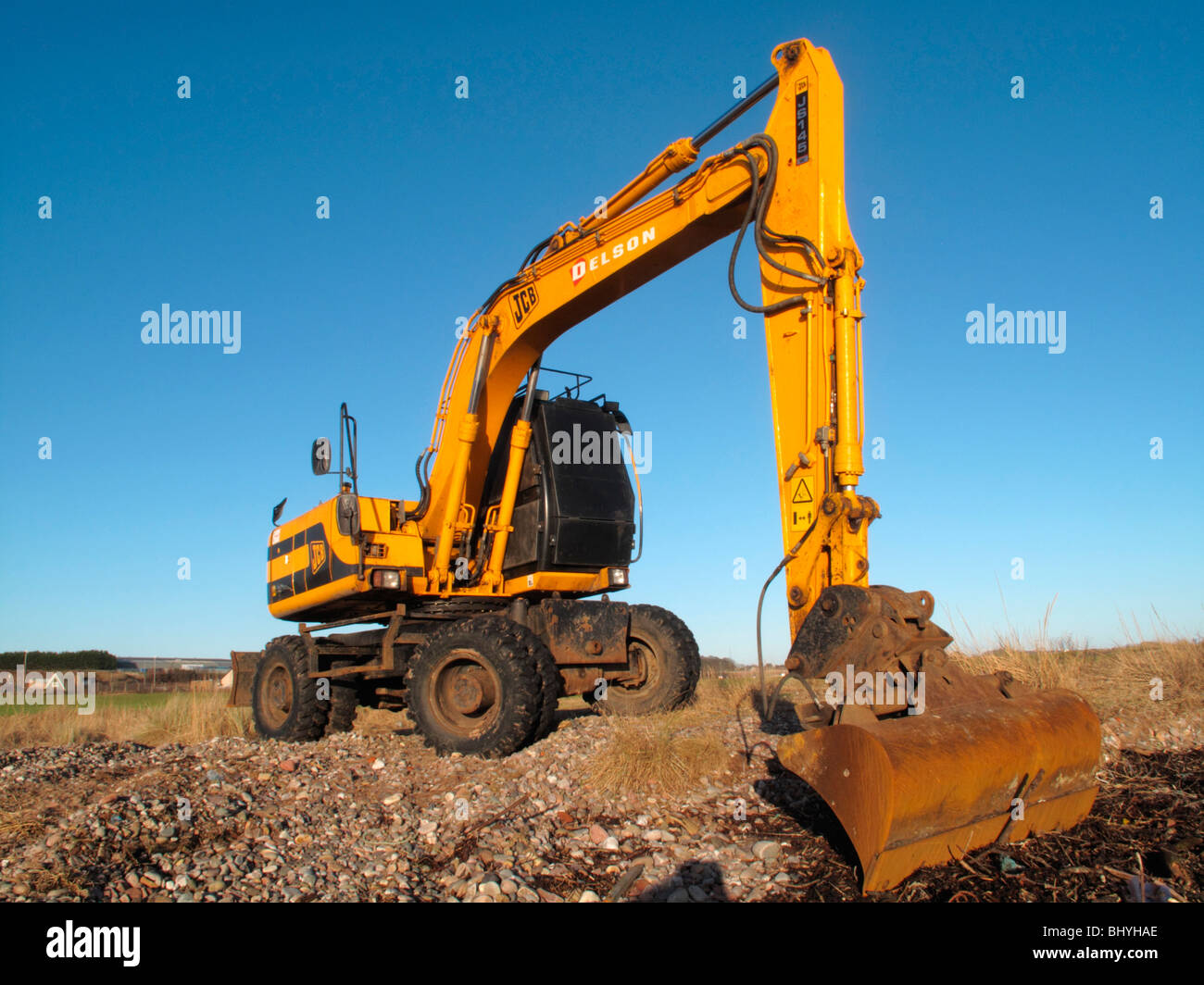 A JCB delson digger clears rubble and rocks from a collapsing river embankment. Stock Photo