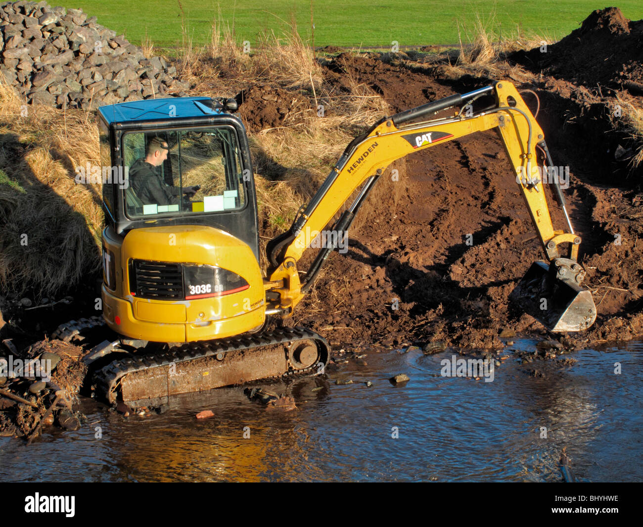 A JC digger clears away falling mud damming up the outflow of a river into the sea. Stock Photo