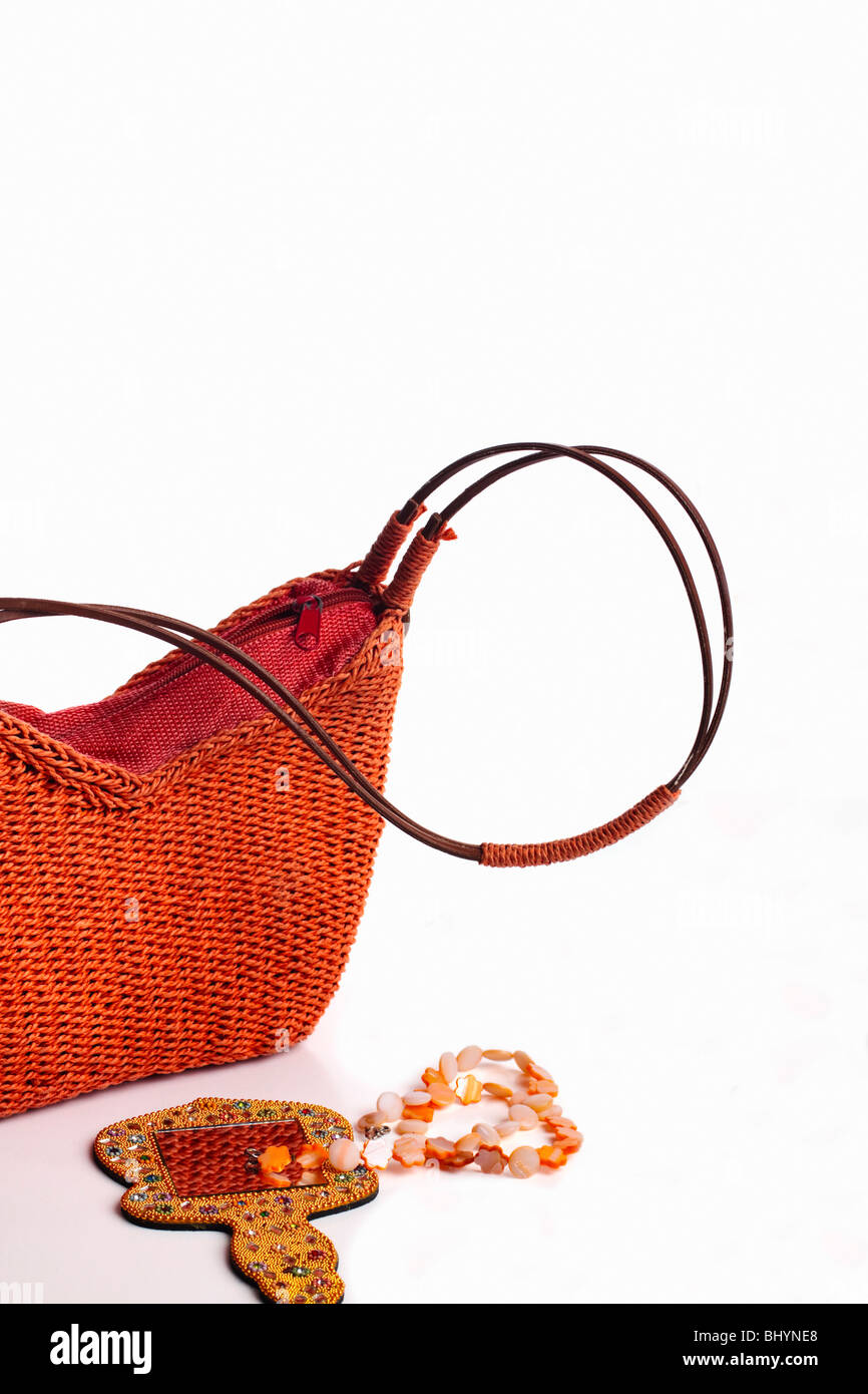 Modern, orange fibre woven handbag with hand mirror and bead necklace. Isolated. Copy space. Stock Photo