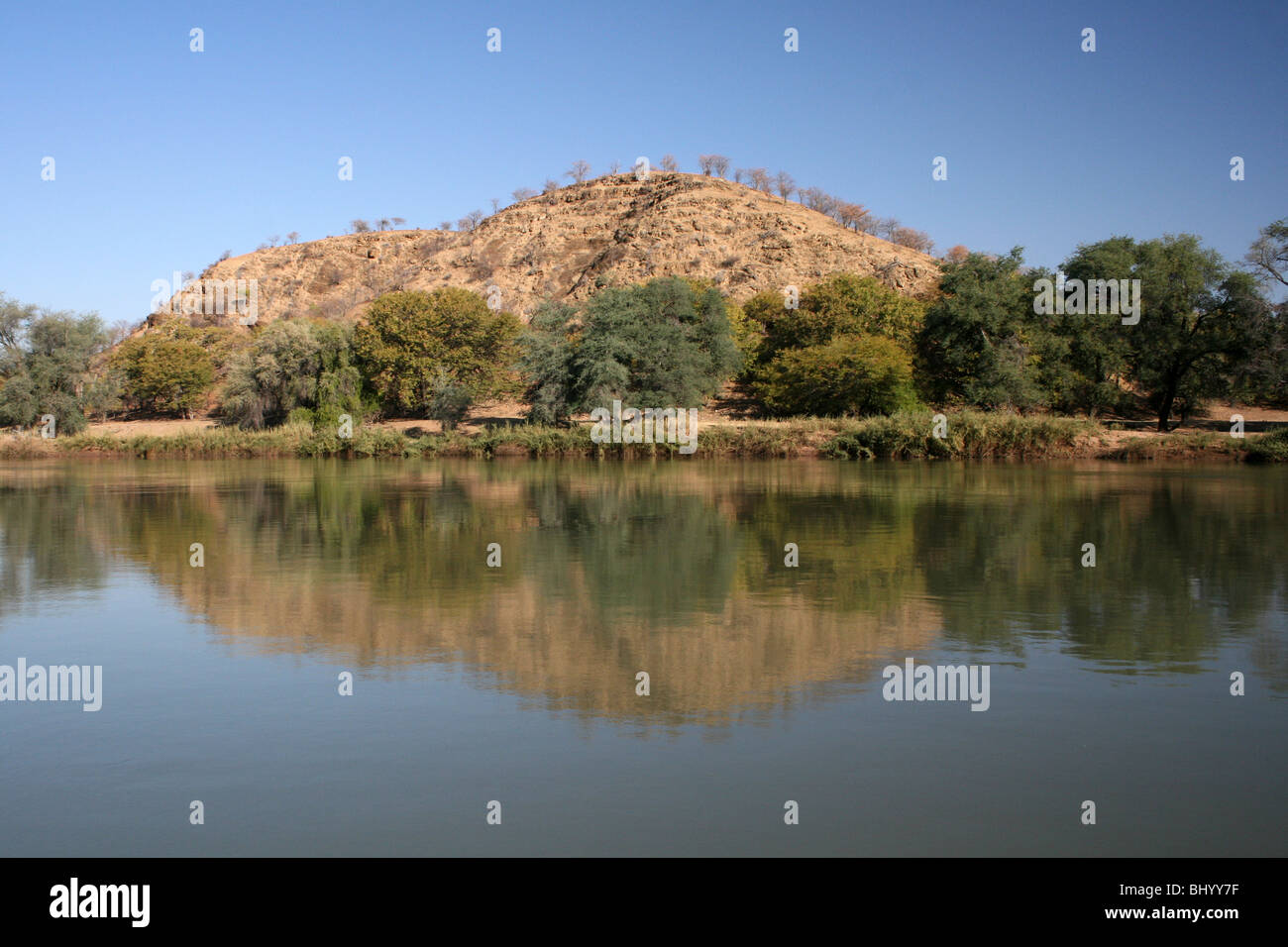 Hill And Trees Reflected In The Kunene River Bordering Namibia and Angola Stock Photo