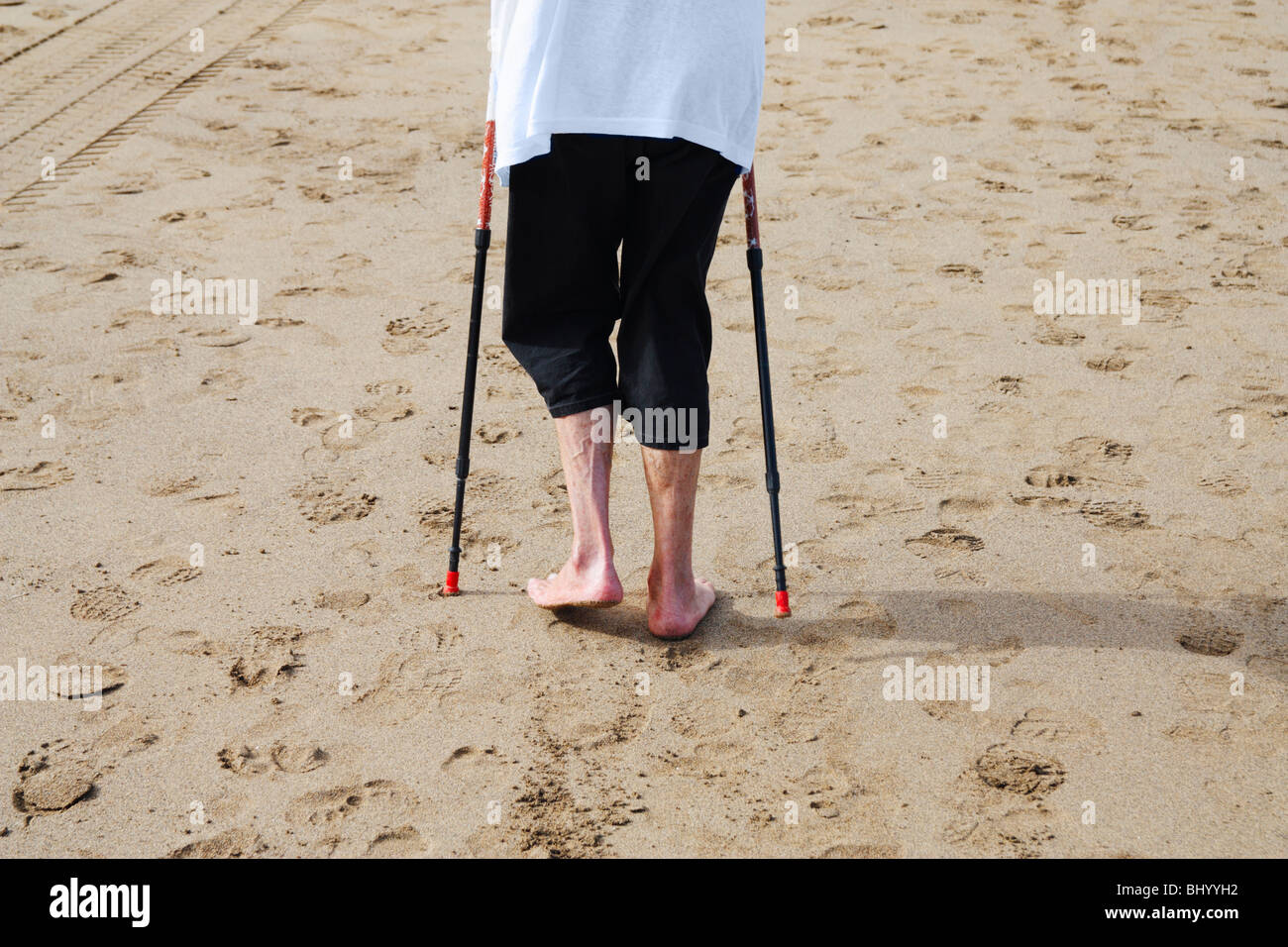 Elderly lady exercising on beach using walking poles Stock Photo