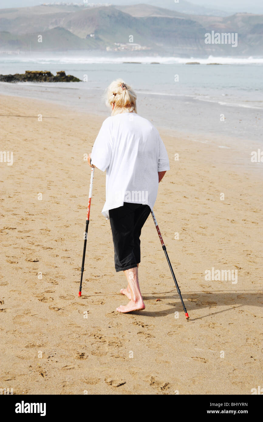 Elderly lady exercising on beach using walking poles Stock Photo