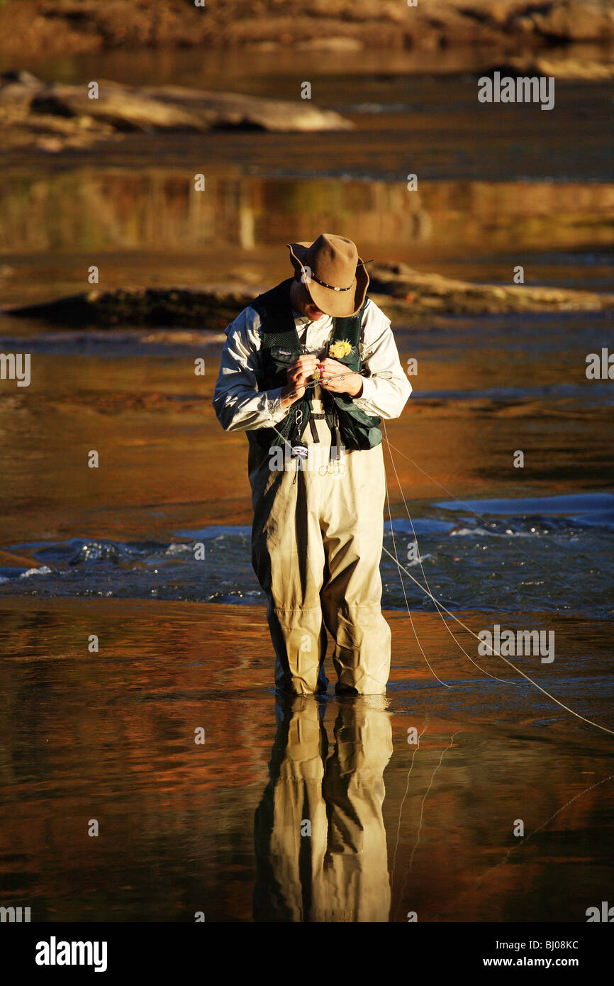 FLY FISHERMAN STANDING IN RIVER WEARING COWBOY HAT TYING ON FLY
