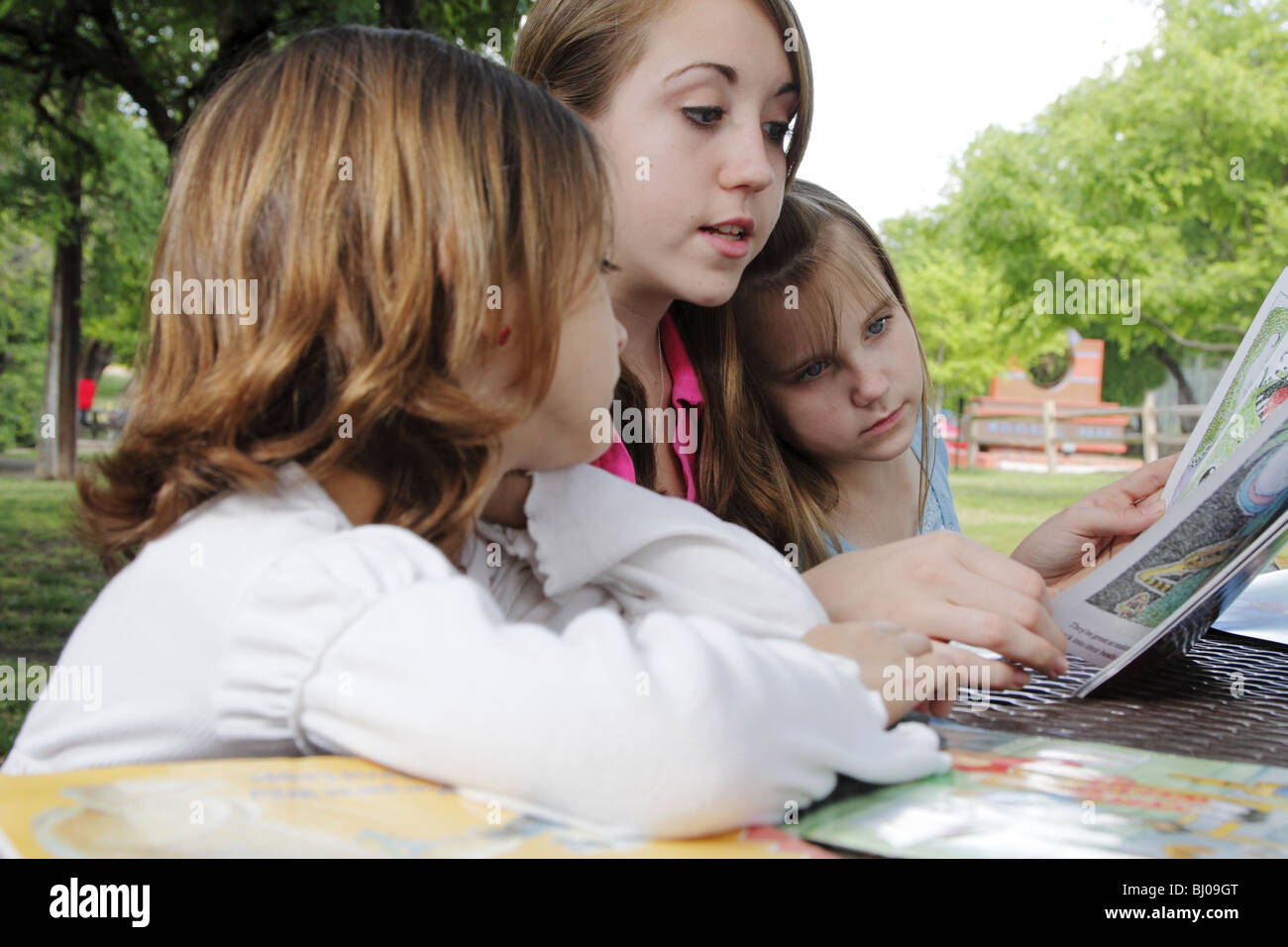 Teen girl reading to two younger girls in the park Stock Photo