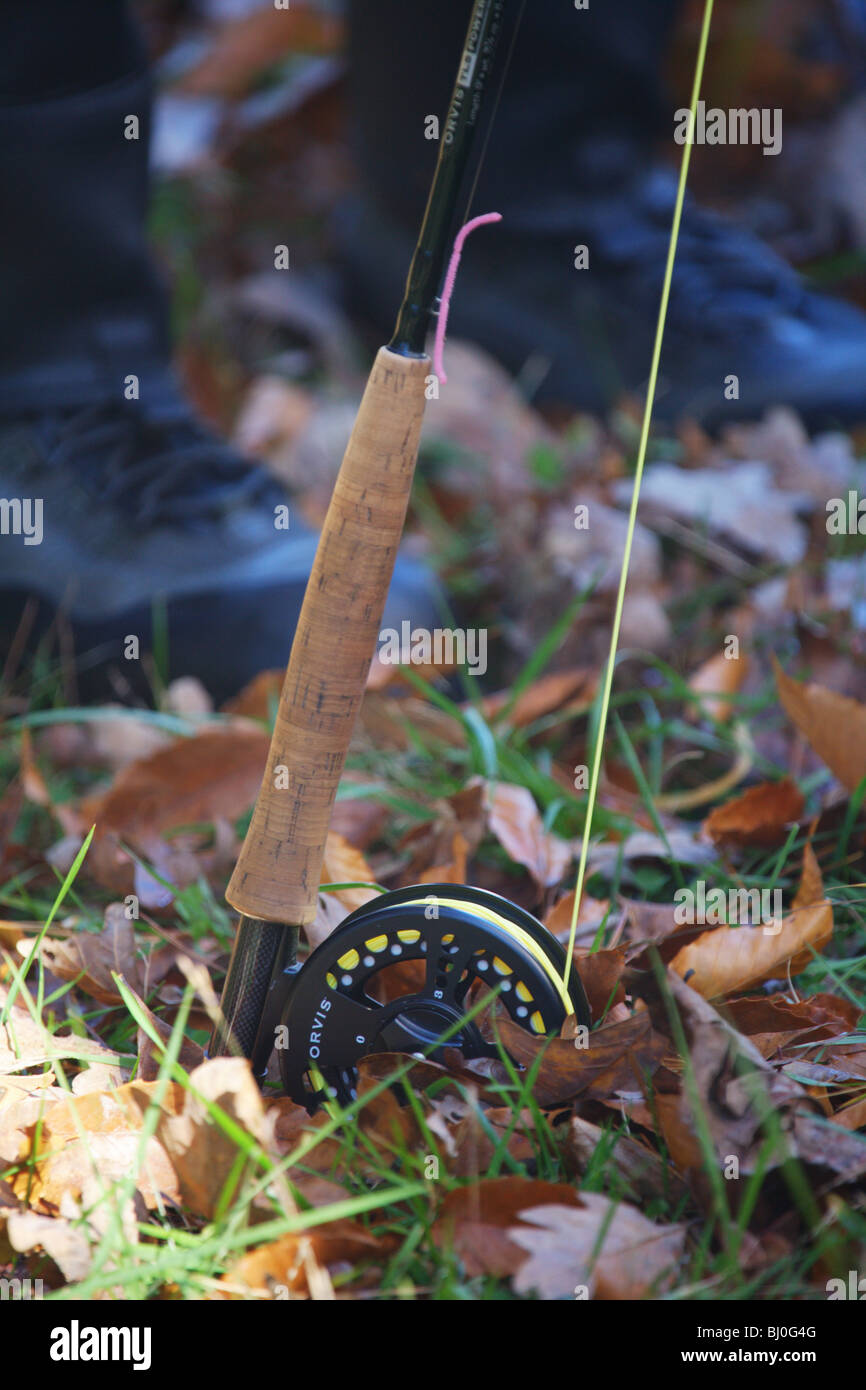 CLOSEUP VIEW ORVIS FLY FISHING ROD REEL SITTING ON LEAVES AT FEET OF FISHERMAN Stock Photo