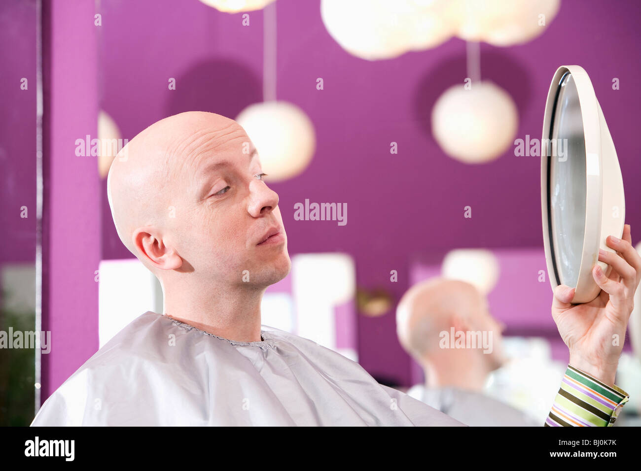 bald man at hair salon looking into mirror Stock Photo