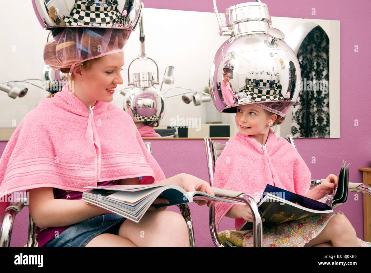 young woman and little girl sitting under hair dryers at hair salon Stock Photo