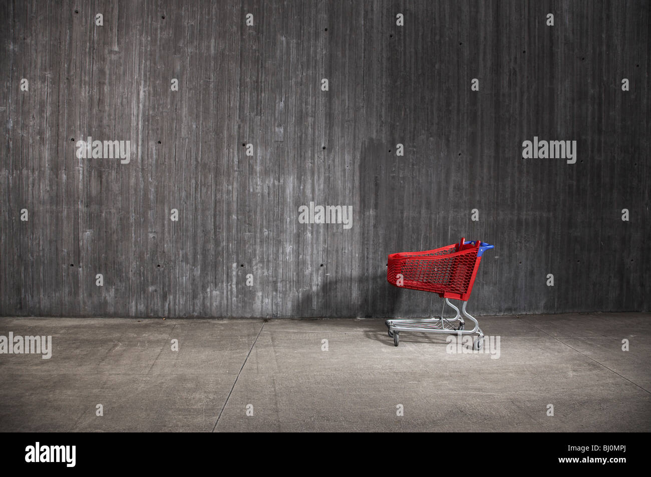 red shopping trolley in front of concrete wall Stock Photo