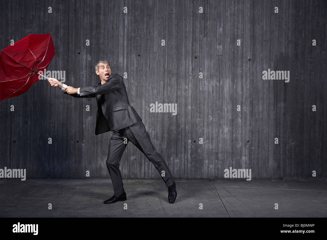 businessman trying to hold red umbrella in stormy weather Stock Photo