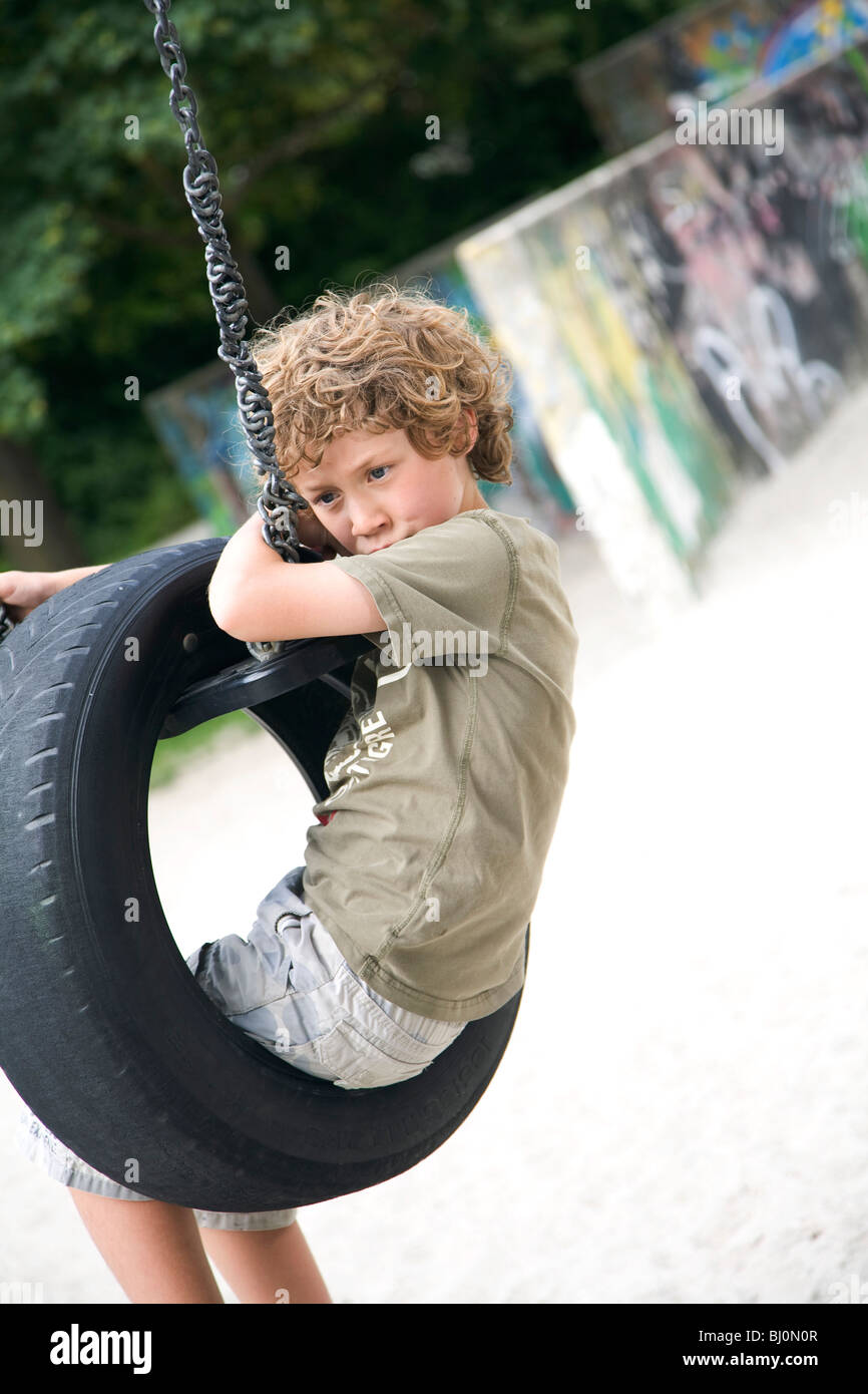young boy sitting on swing at playground Stock Photo