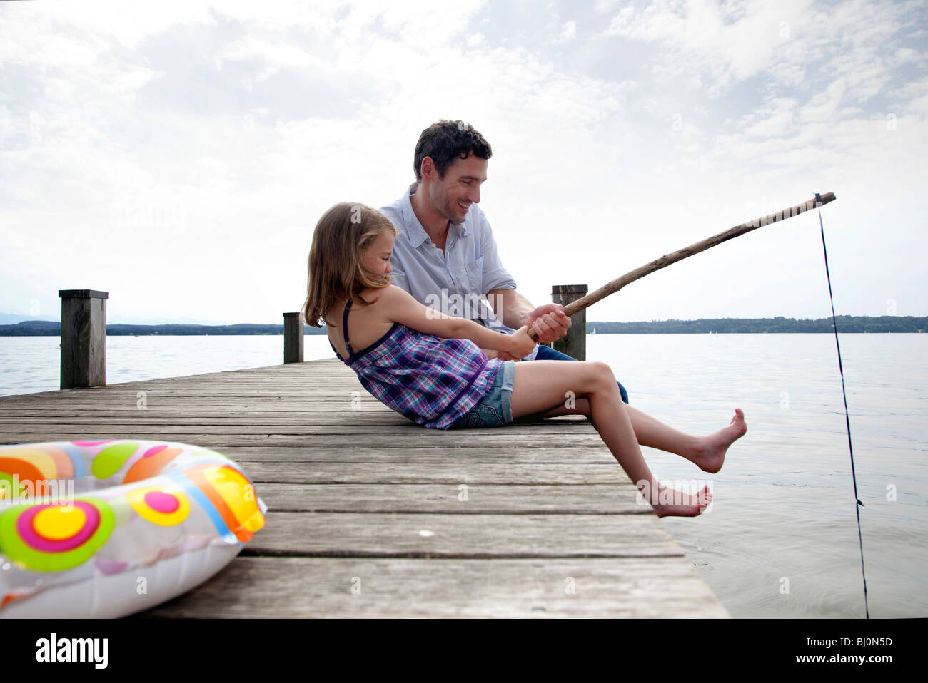 father and daughter on pier angling together Stock Photo