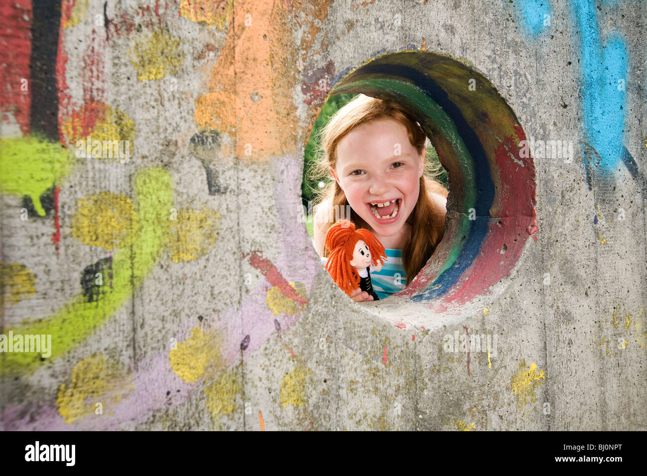 portrait of laughing girl looking through hole in wall on playground Stock Photo