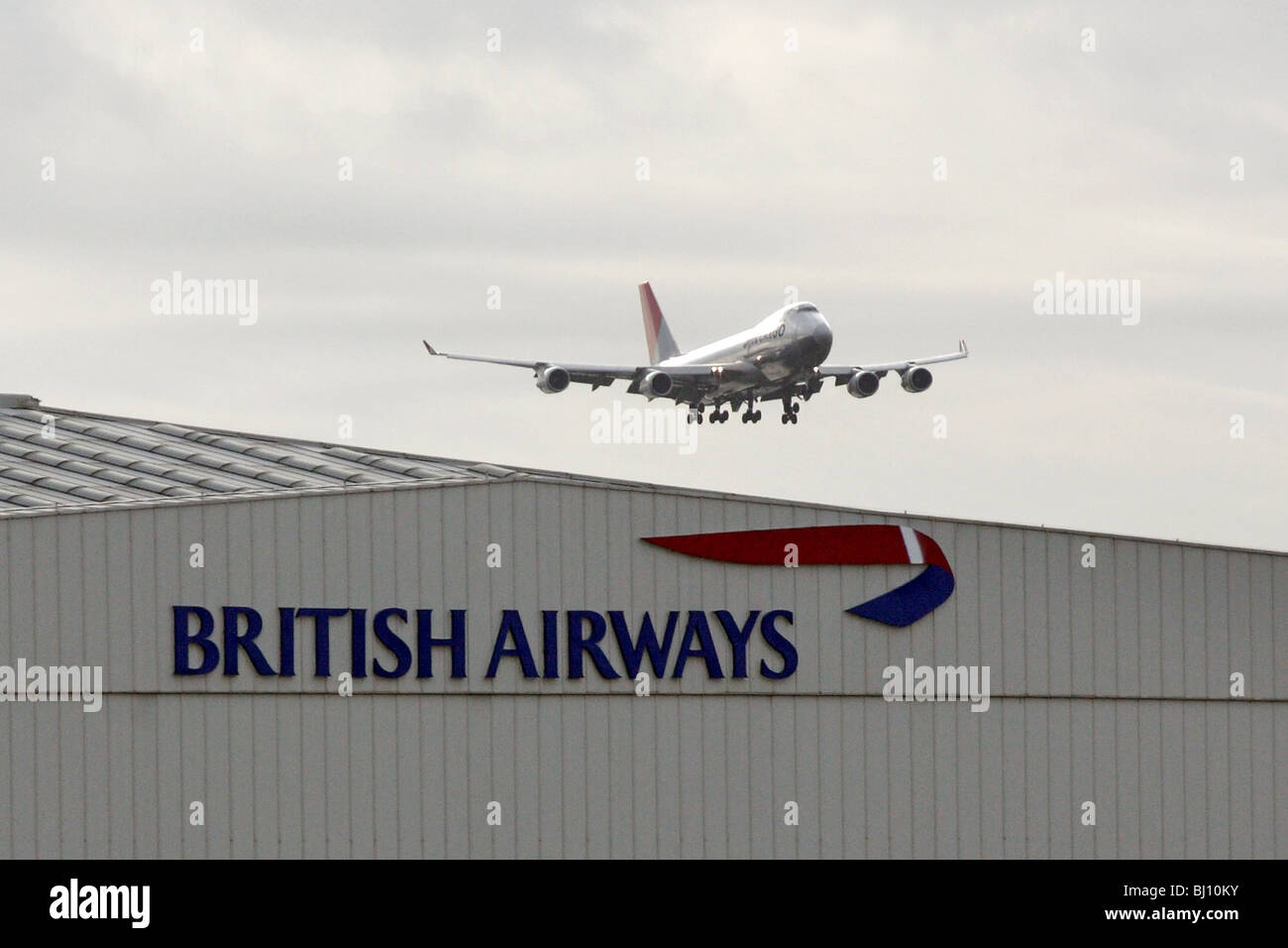 A passenger plane flying over a hangar of the British Airways, London, Great Britain Stock Photo