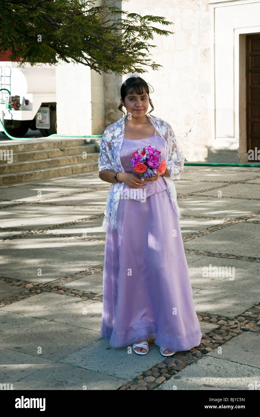 pretty Mexican teen standing in plaza outside Santo Domingo Church wearing  gown for her Quinceanera ceremony & holding flowers Stock Photo