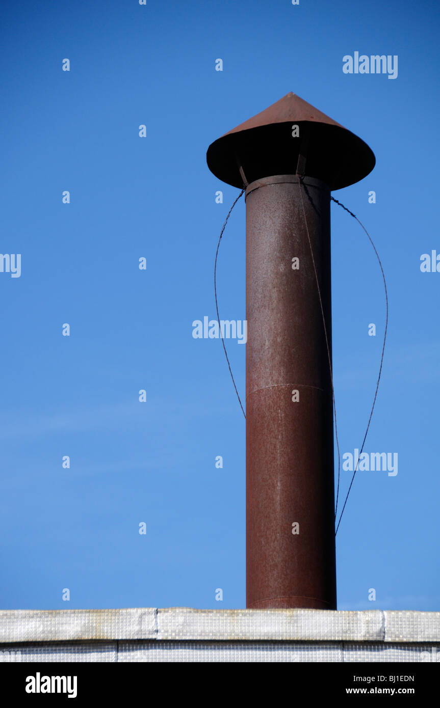 Stock photo of an old rusting metal stove pipe sticking out the roof of