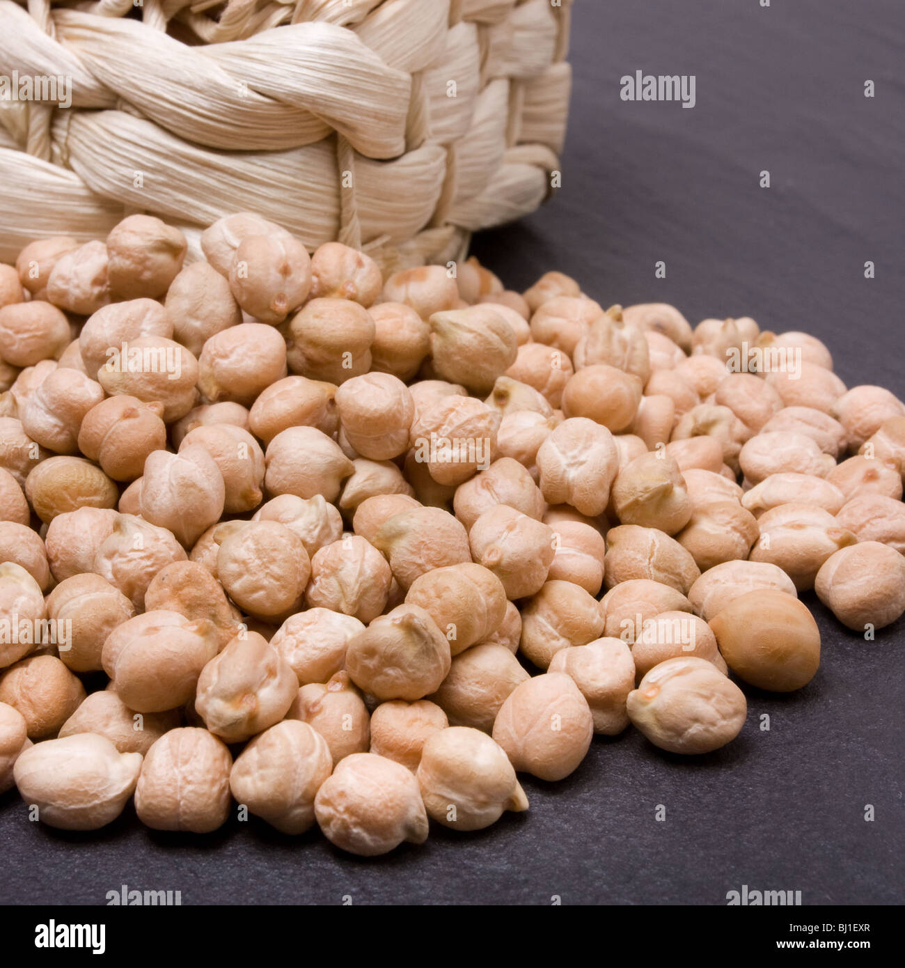 Dried chick peas overflowing from wicker basket against dark slate background. Stock Photo