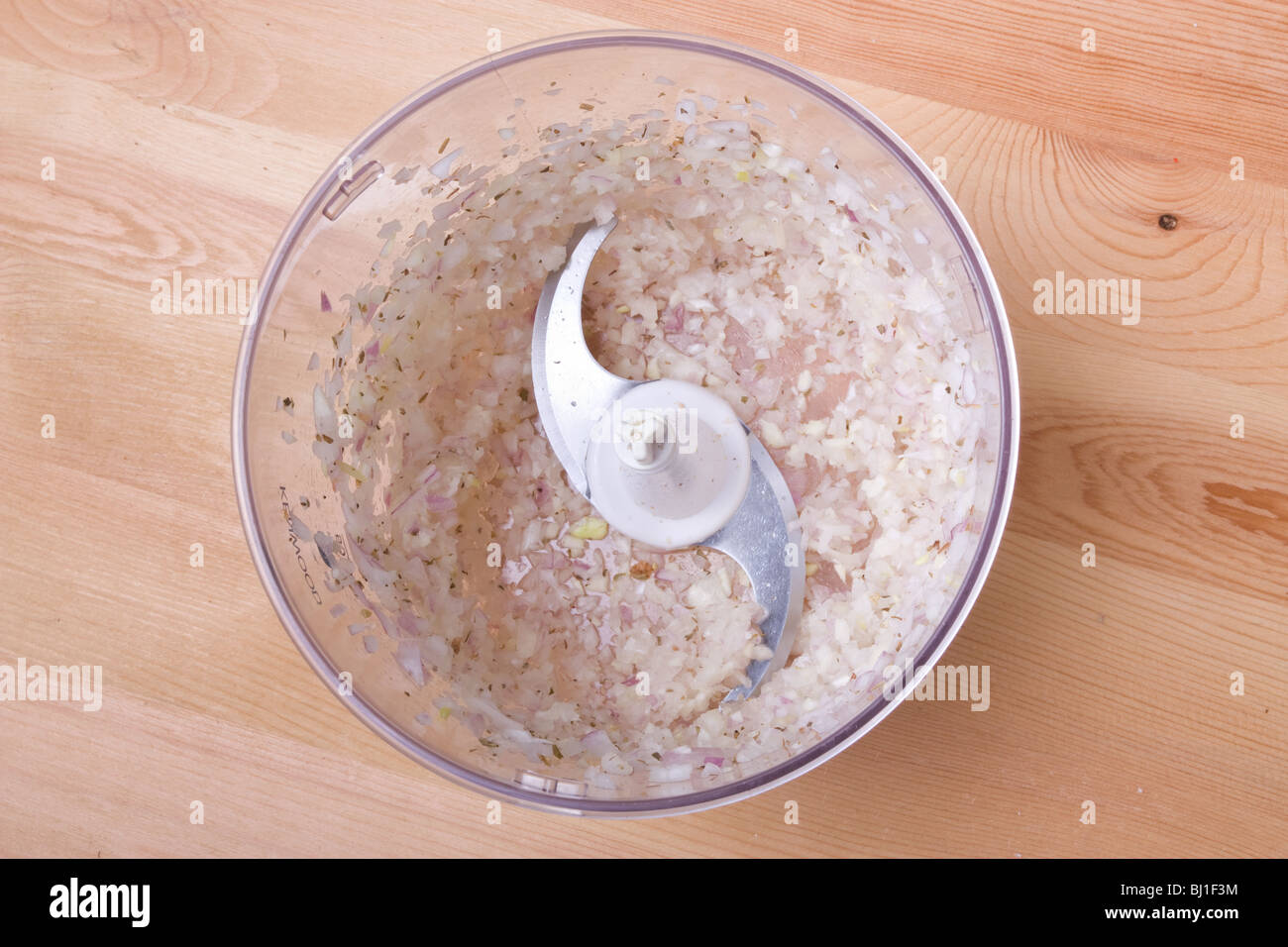 Finely chopped food processed shallot in plastic container on wooden work surface. Stock Photo