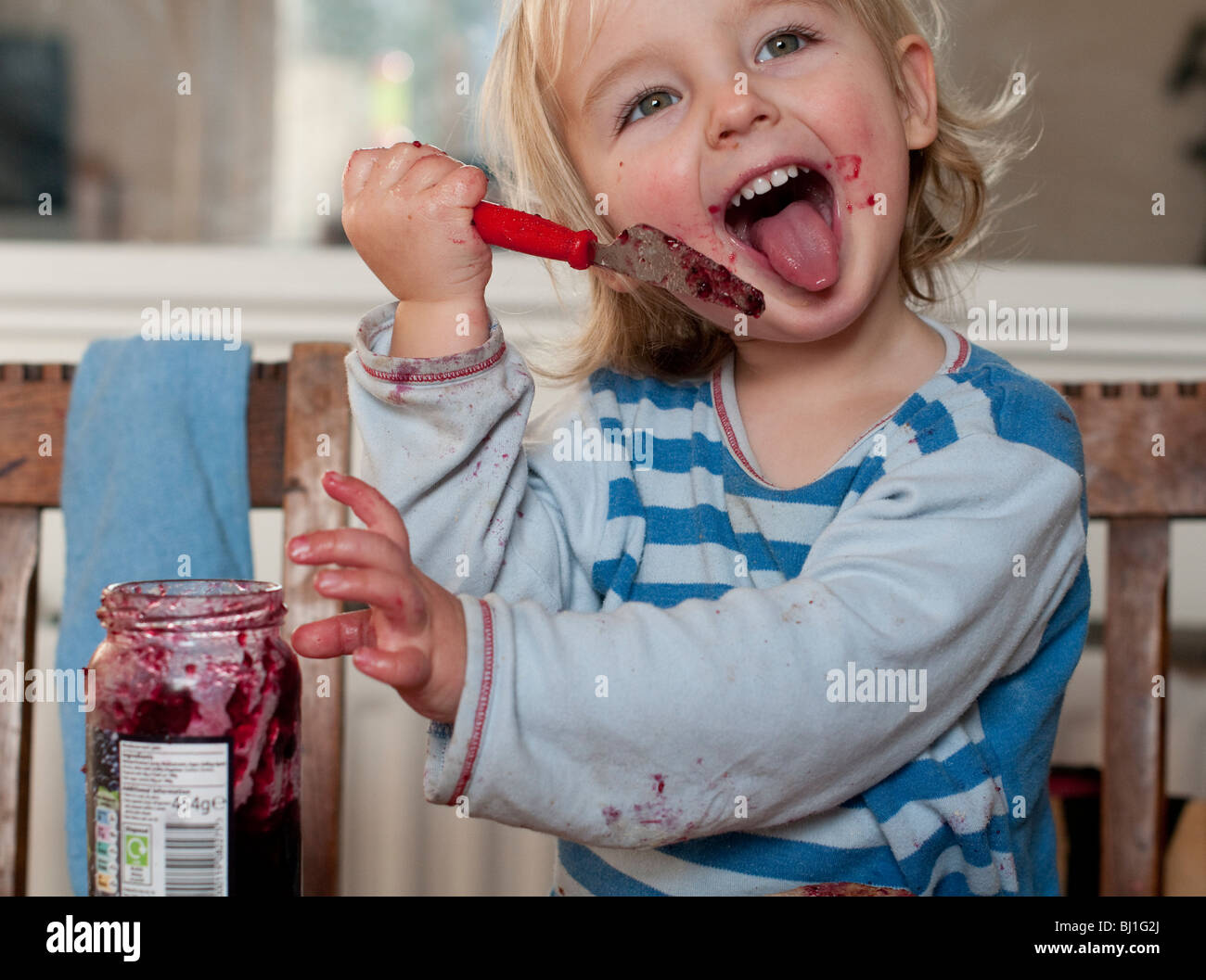 A young boy with no manners, smiles as he licks jam from his knife at the breakfast table Stock Photo