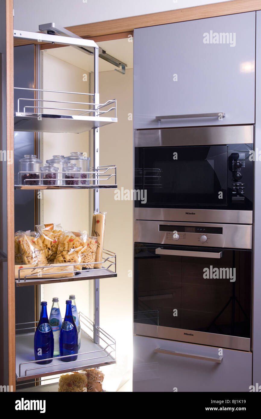 Gray kitchen cabinet with extensible steel shelves for food storage and electric oven and microwave Stock Photo