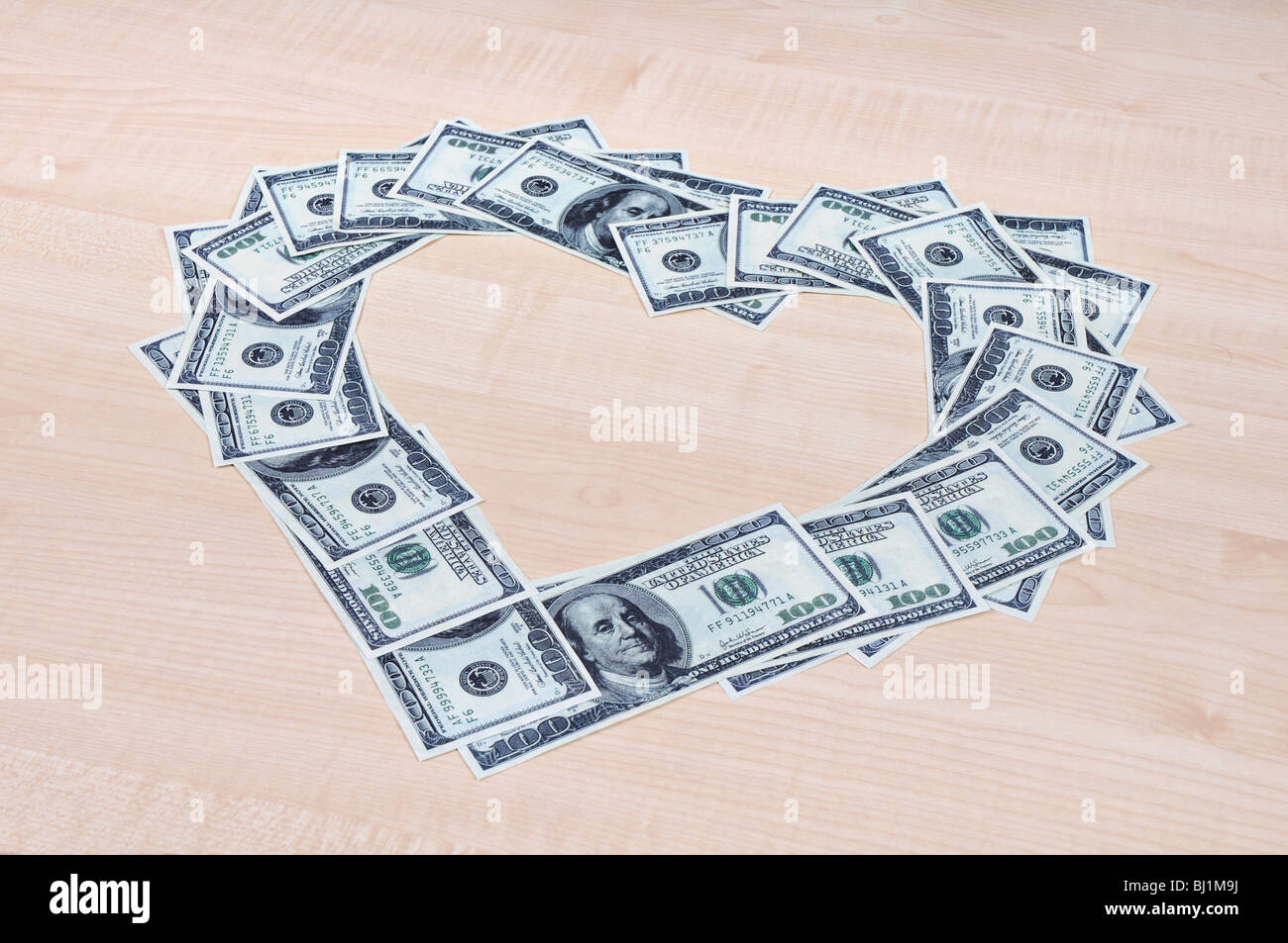 Heart symbol made of 100 dollar bills lying on a table. Stock Photo