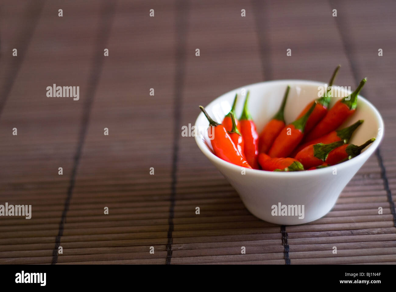 A small white serving bowl of whole red chillis on a bamboo surface Stock Photo