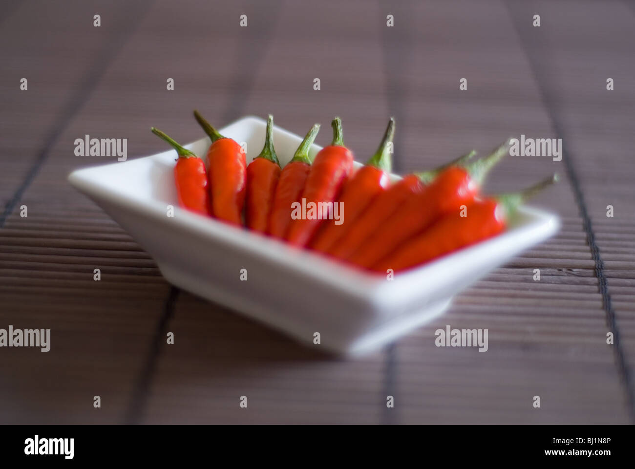 An Asian style square bowl of whole red chillis on a bamboo surface Stock Photo