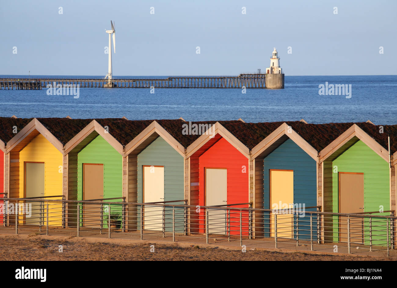 Beach huts at Blyth in Northumberland, England with the pier and a wind turbine in the background. Stock Photo