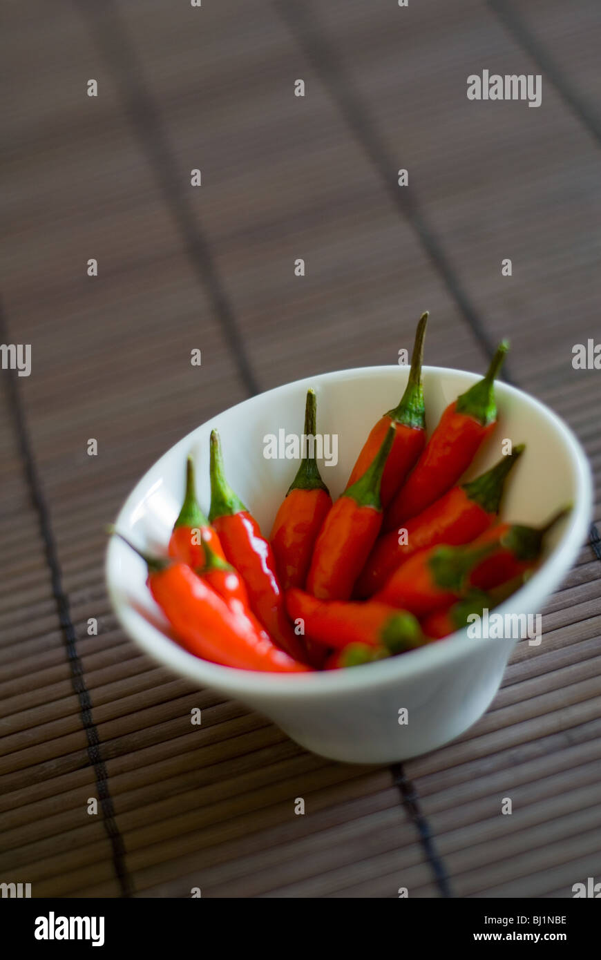 A white bowl of whole red chillis on a bamboo surface Stock Photo