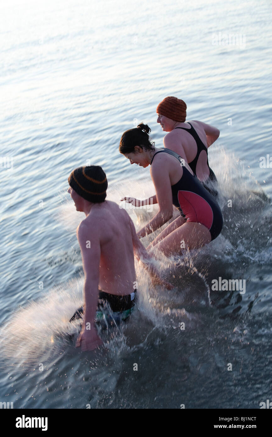 Three young university students jumping into the sea on a very cold March evening, Aberystwyth Wales UK Stock Photo