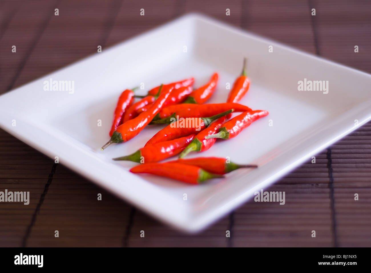 A square white plate of whole red chillis on a bamboo surface Stock Photo