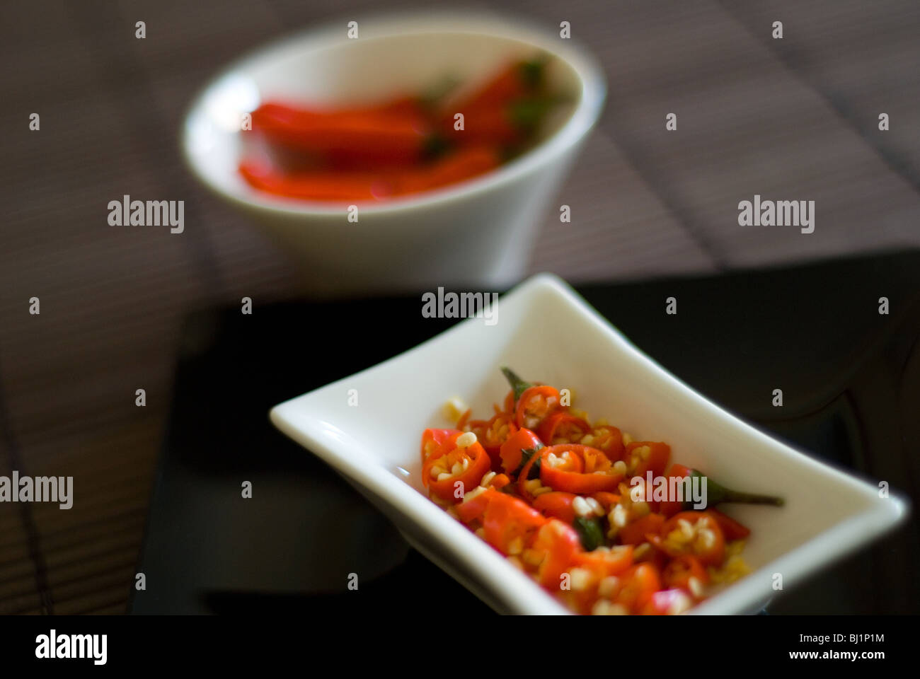 An Asian style serving bowl of chopped red chillis with whole chillis in a bowl in the background Stock Photo