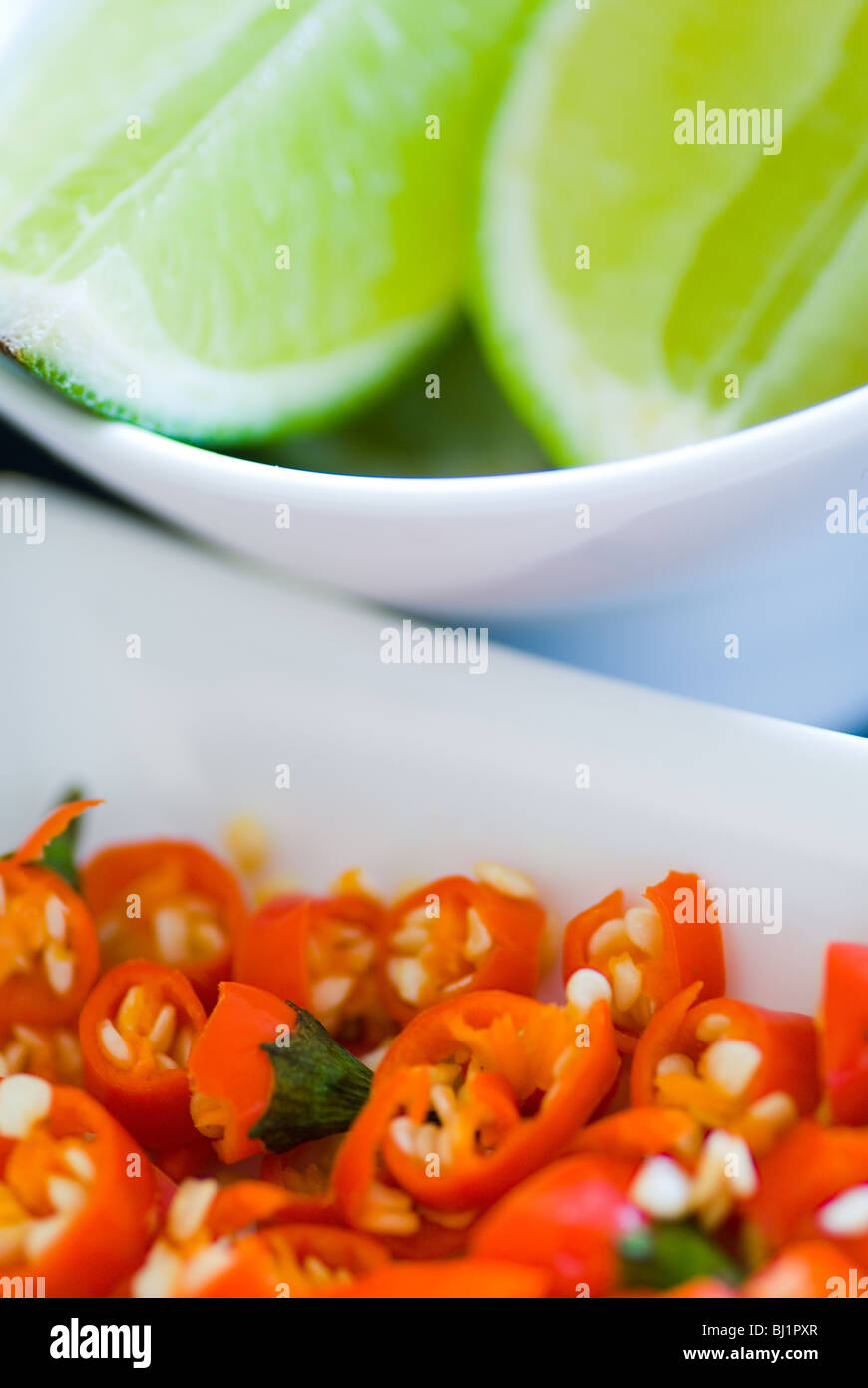 Small serving bowls with chopped red chillis and wedges of Lime Stock Photo