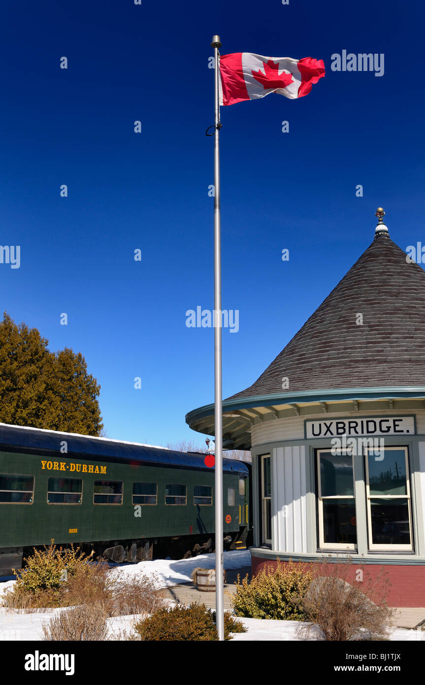 The Uxbridge Ontario train station in winter with Canadian flag and a York Durham Heritage Railway car with blue sky Stock Photo