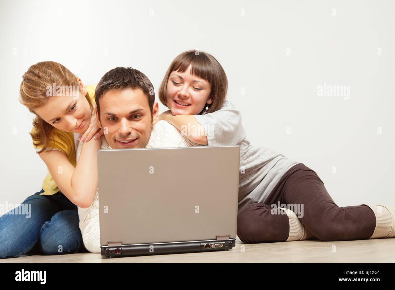 Group Of Three Happy People Lying On The Floor With Laptop