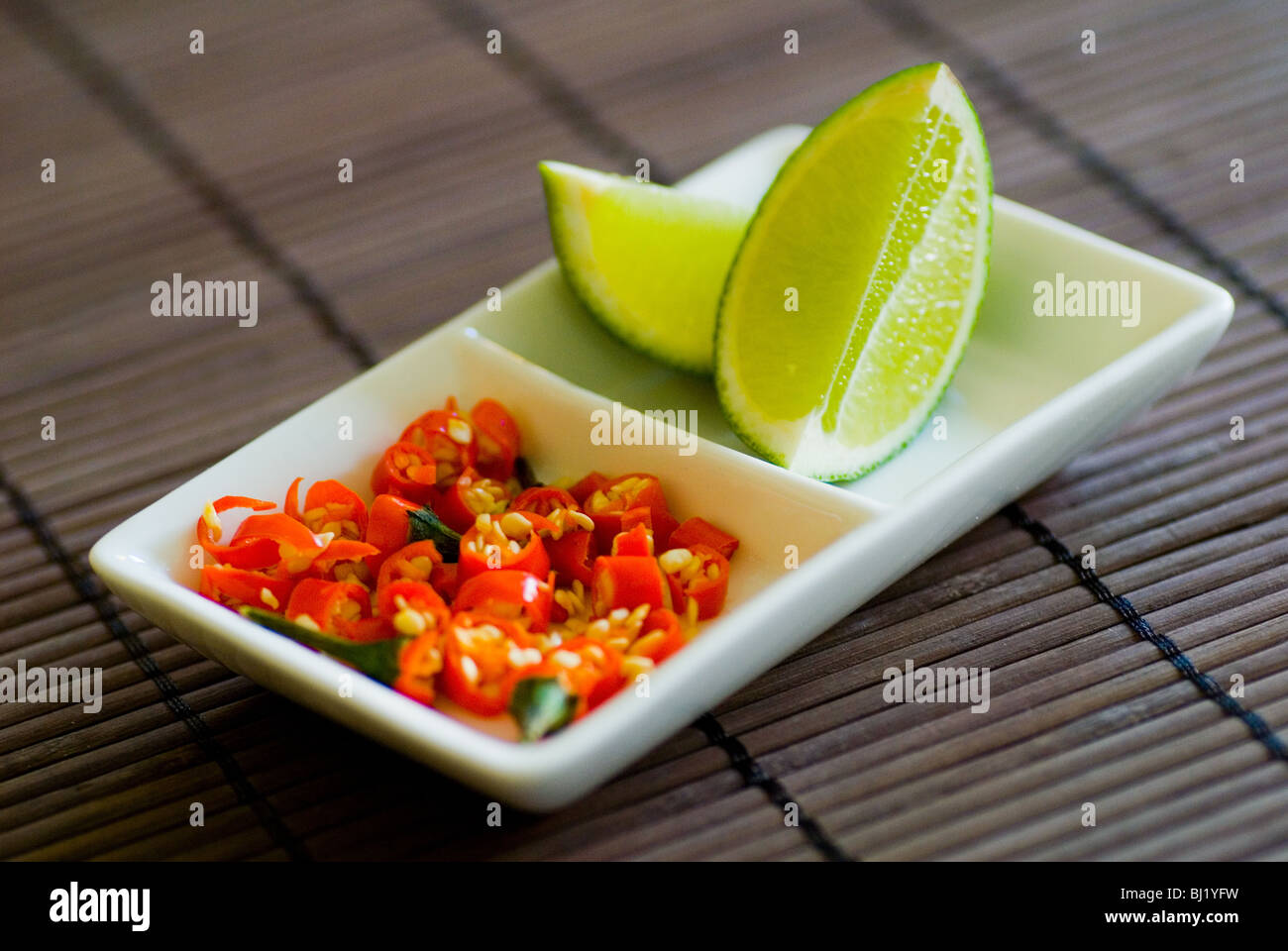 A small serving dish with Red Chillis and Lime on a bamboo surface Stock Photo