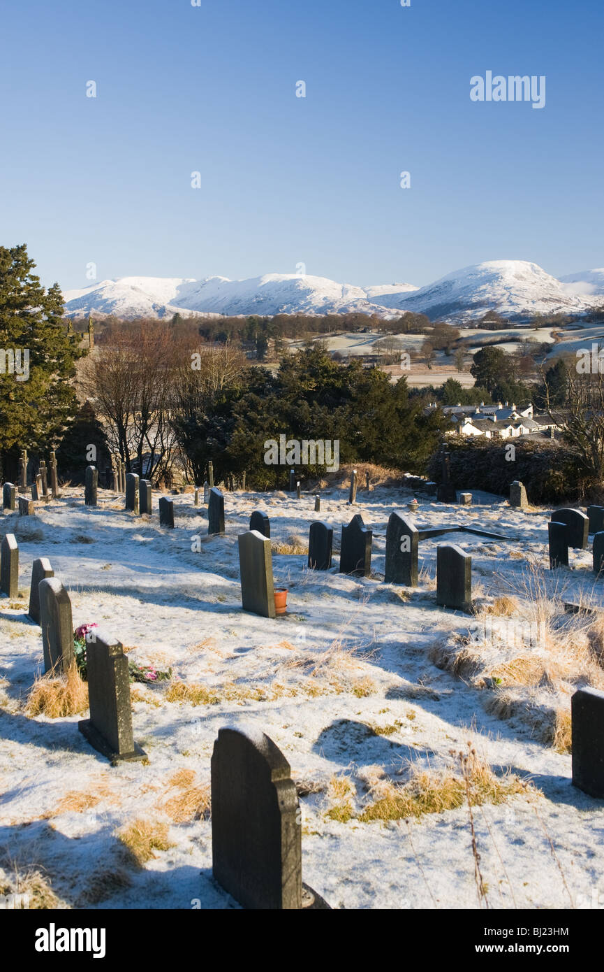 Grave Stones in Hawkshead Church Graveyard with Snow Covered Cumbrian Mountains Lake District Cumbria England United Kingdom UK Stock Photo