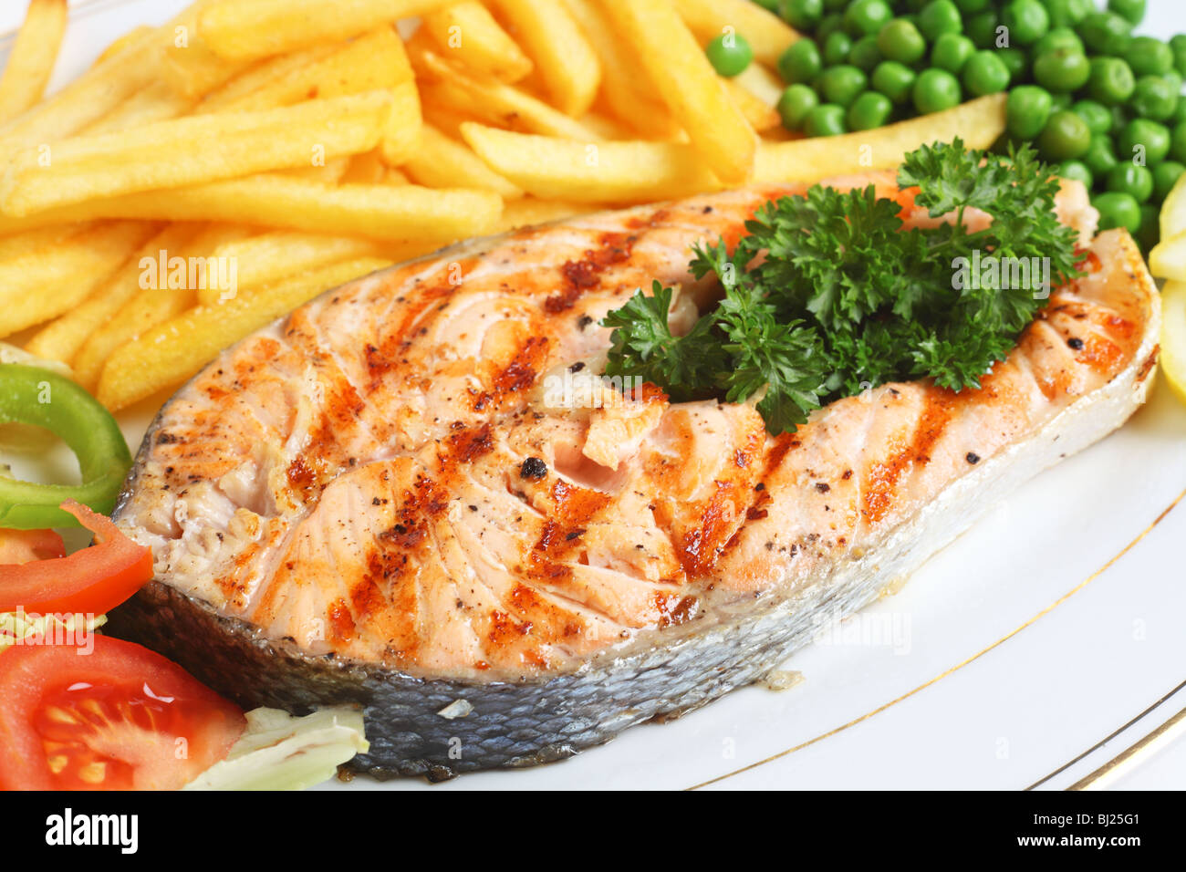 A close-up view of a grilled salmon steak served with salad, chips ...