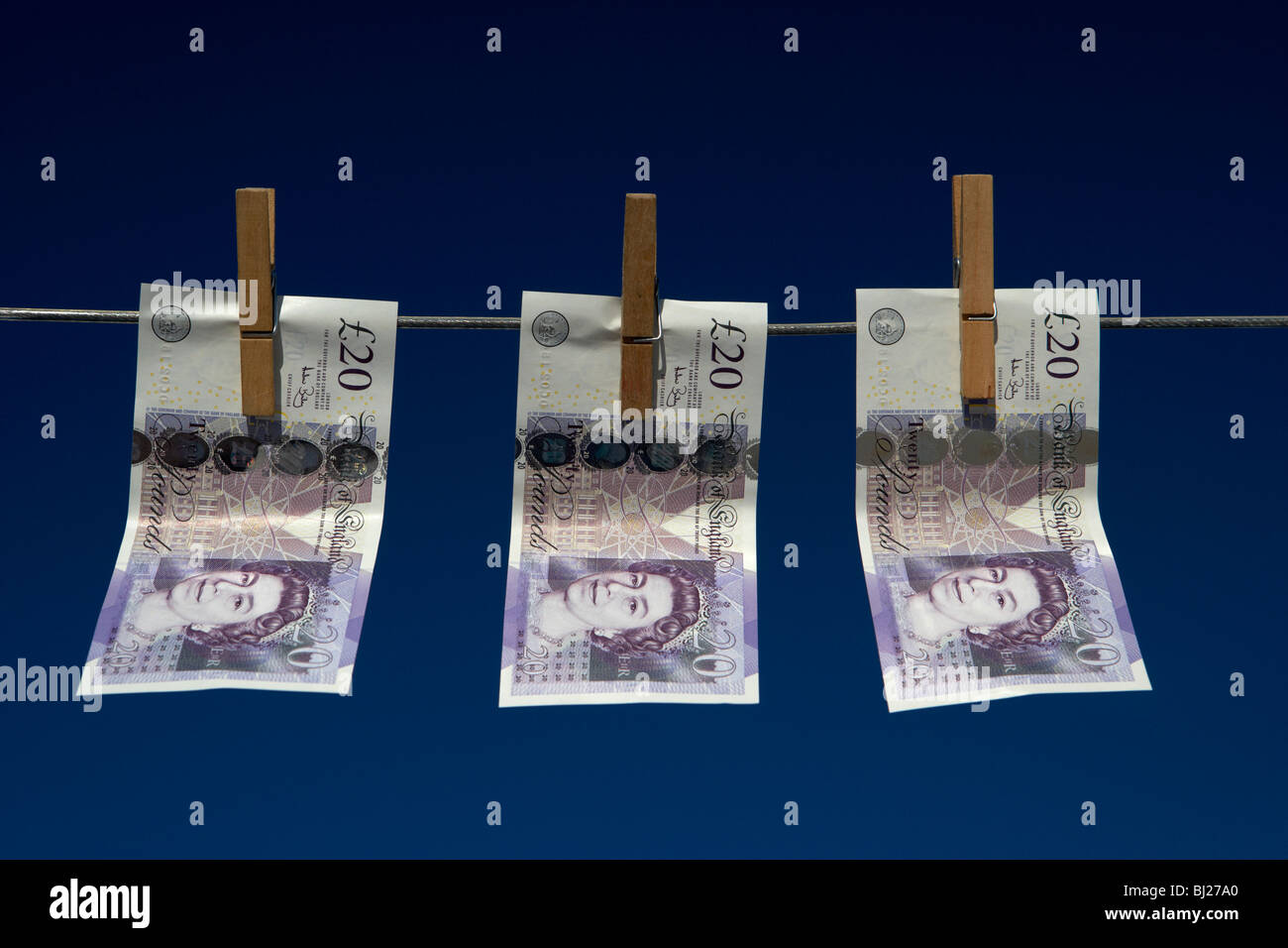 three twenty pounds sterling banknotes hanging on a washing line with blue sky Stock Photo