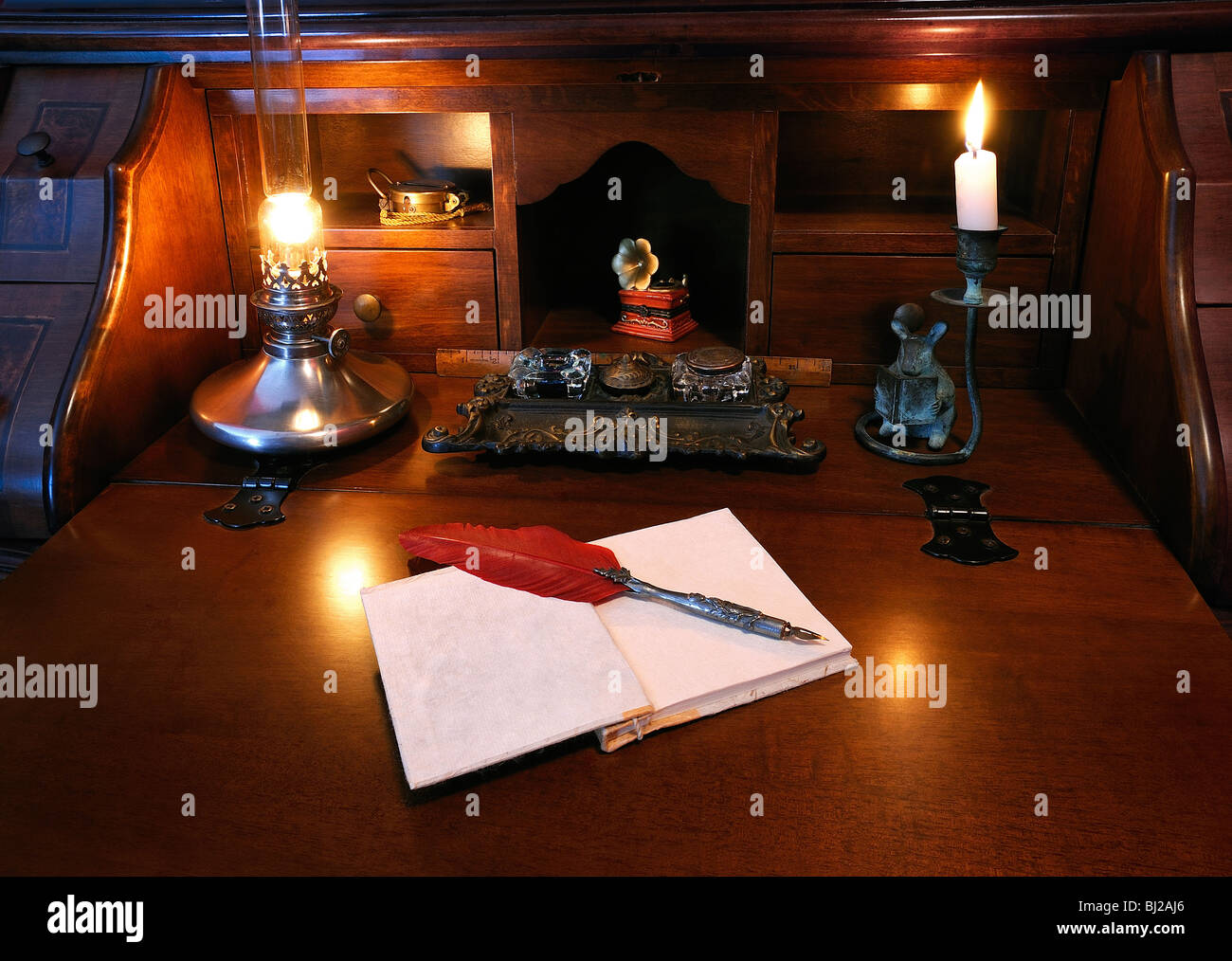 Antique writing desk with red feather quill pen and oil lamp. Ink well in center. Stock Photo