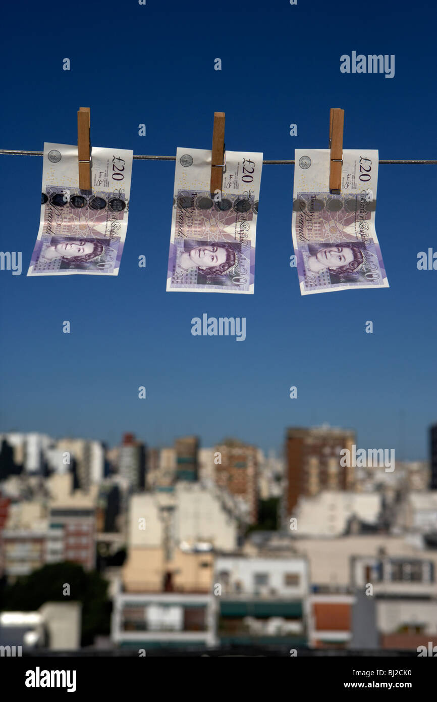 three twenty pounds sterling banknotes hanging on a washing line with blue sky above a city skyline Stock Photo