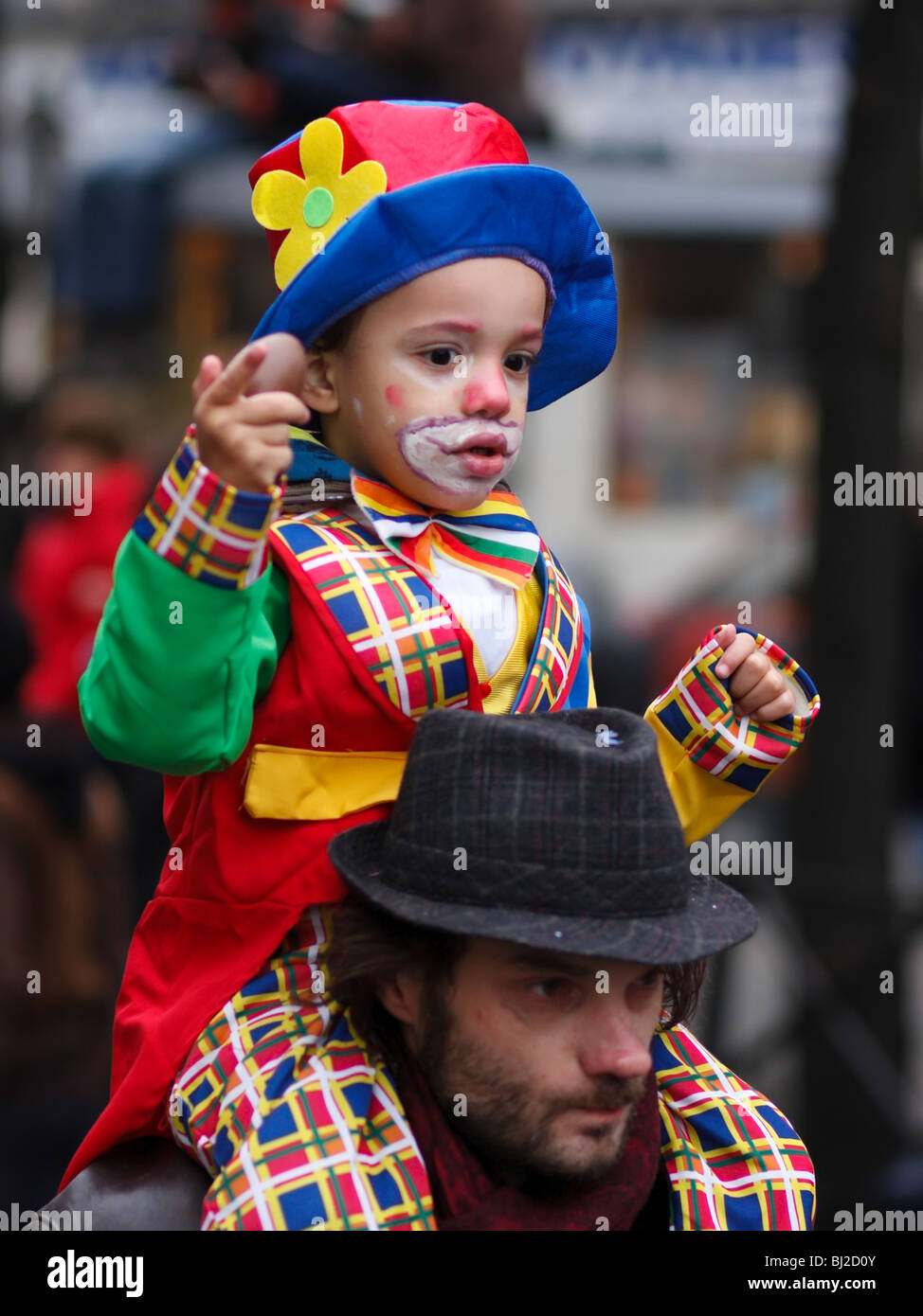 A child in clown costume sitting on his father's shoulders, looking at